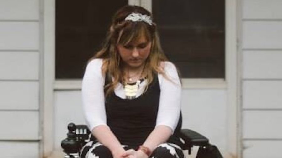 Ariella Barker sitting in a wheelchair in front of her house, looking down