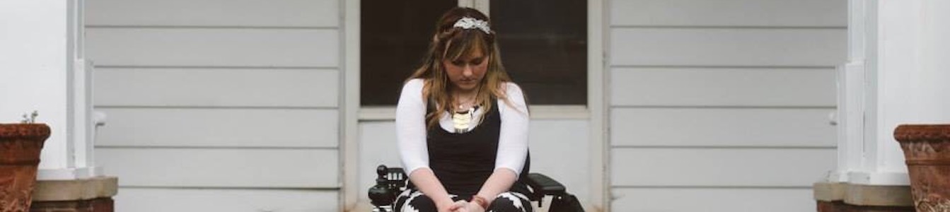 Ariella Barker sitting in a wheelchair in front of her house, looking down