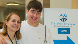 Lisa Handelman smiles with a young adult with a disability in front of a sign for The Jewish Federation of Greater Washington
