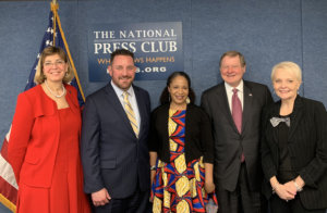 L-R: Jennifer Laszlo Mizrahi, Aaron Dorfman, Kerrien Suarez, Steve Bartlett and Stephanie Powers smiling in front of a sign for the National Press Club (Where News Happens Press.org), an American flag, and a blue wall