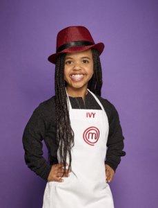 Ivy wearing her MasterChef Junior Jacket, smiling in front of a plain purple wall