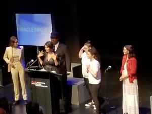 Robia Rashid speaking at a podium surrounded by cast members of Atypical