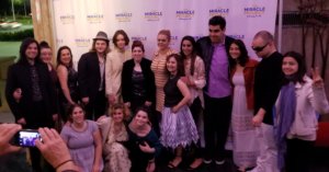 A group of cast members with Elaine Hall posing for a picture in front of a banner saying The Miracle Project