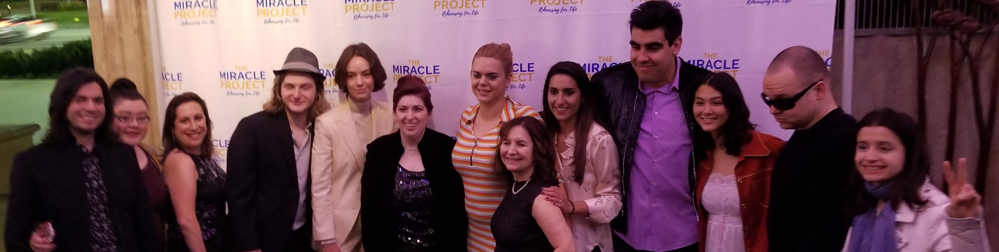 A group of cast members with Elaine Hall posing for a picture in front of a banner saying The Miracle Project