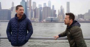Warren Christie and Kurt Yaeger talking on The Village in front of the Hudson River with New York City's skyline in the background
