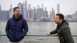 Warren Christie and Kurt Yaeger talking on The Village in front of the Hudson River with New York City's skyline in the background