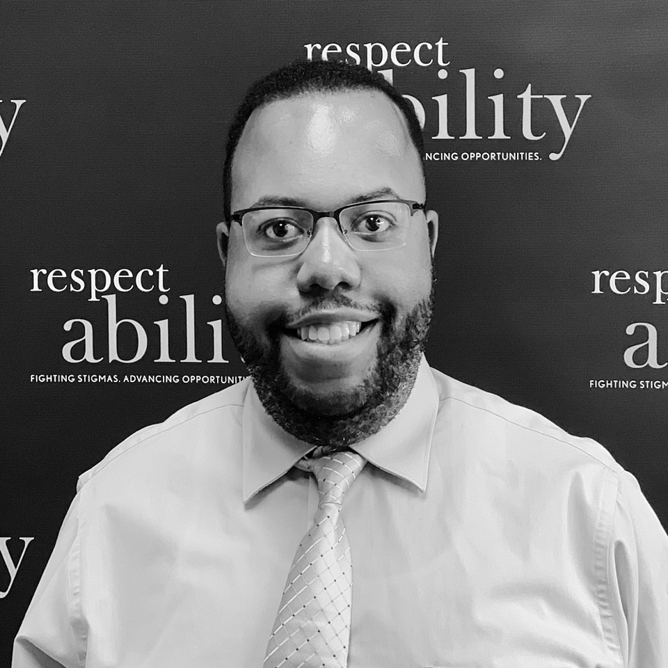 Anthony Rendolph Clarke Brown II smiling in front of the RespectAbility banner