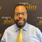 Anthony Rendolph Clarke Brown II smiling in front of the RespectAbility banner