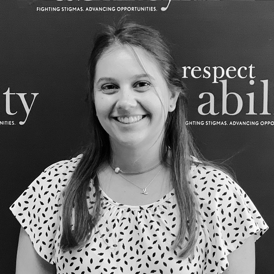 Elizabeth Batwinis, smiling in front of the RespectAbility banner