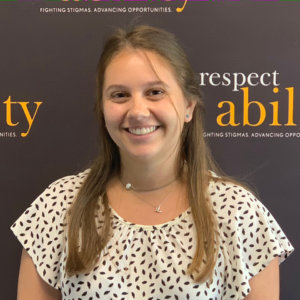 Elizabeth Batwinis smiling in front of the RespectAbility banner