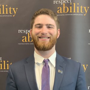 Adam Fishbein smiling in front of the RespectAbility banner