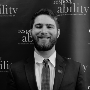 Adam Fishbein smiling in front of the RespectAbility banner