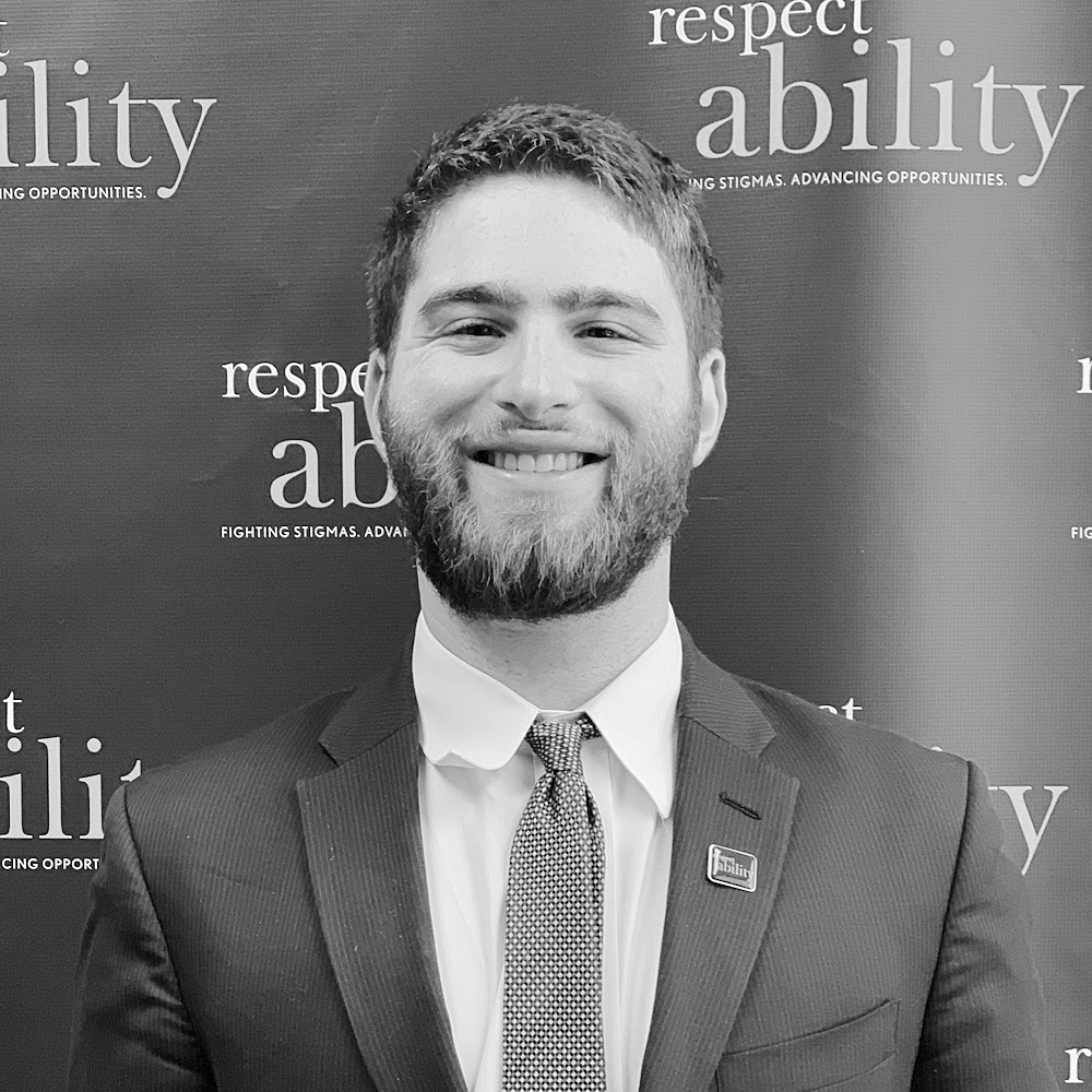 Adam Fishbein smiling in front of the RespectAbility banner