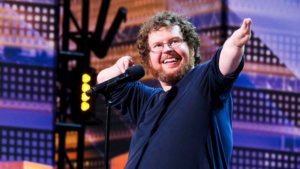 Ryan Niemiller on stage on America's Got Talent. Niemiller has a disability in both of his arms.