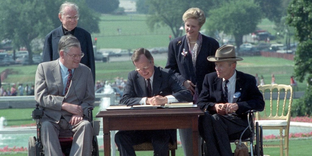 George H.W. Bush signs the ADA into law with four people around him, two of whom are wheelchair users