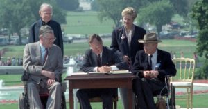 George H.W. Bush signs the ADA into law with four people around him, two of whom are wheelchair users