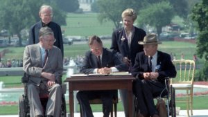 George H.W. Bush signs the ADA into law with four people around him, two of whom are wheelchair users
