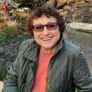 Ila Eckhoff smiling outside in front of trees and plants wearing glasses