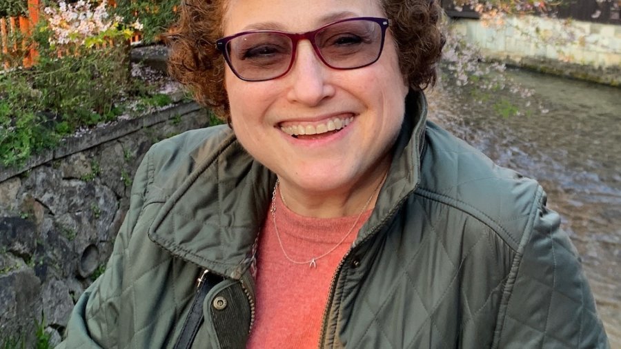 Ila Eckhoff smiling outside in front of trees and plants wearing glasses