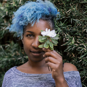 Tchaiko Omawale holding a flower in front of her face, smiling