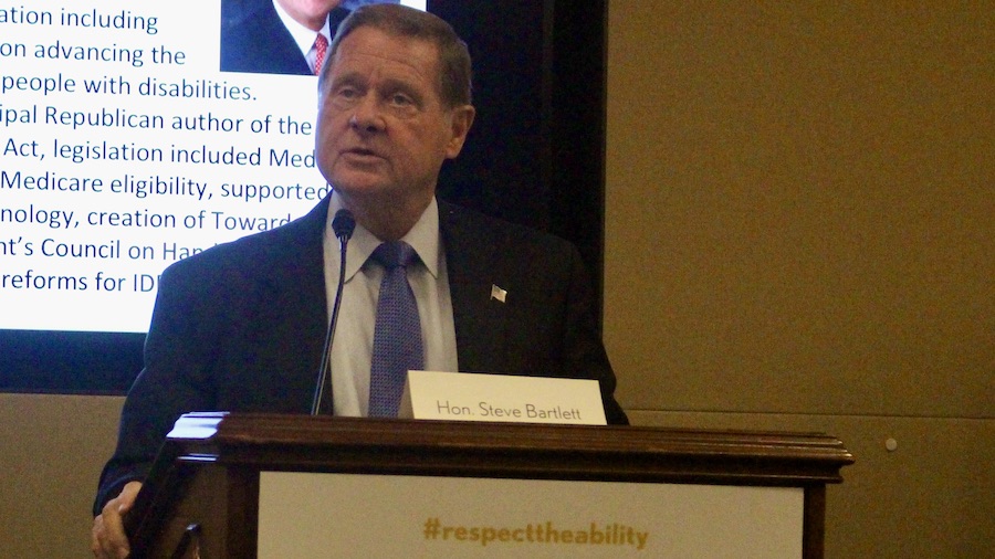 Steve Bartlett speaking in front of a screen with his biography on it behind a podium with #RespectTheAbility on it