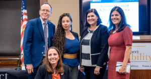 Top row L-R: Jonathan Murray, Nasreen Alkhateeb, Lauren Appelbaum and Teresa Hammond. Candace Cable in second row. All are smiling together in front of RespectAbility's podium, screen, and an American flag