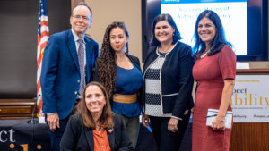 Top row L-R: Jonathan Murray, Nasreen Alkhateeb, Lauren Appelbaum and Teresa Hammond. Candace Cable in second row. All are smiling together in front of RespectAbility's podium, screen, and an American flag