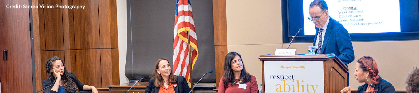 L-R: Nasreen Alkhateeb, Candace Cable, Teresa Hammond and Jonathan Murray. Jonathan is behind a podium while the three women are sitting behind a table in front of an American flag. Credit: Stereo Vision Photography