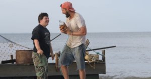 Zak (Zack Gottsagen), left, and Tyler (Shia LaBeouf), right, near a raft they built in “The Peanut Butter Falcon”