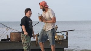 Zak (Zack Gottsagen), left, and Tyler (Shia LaBeouf), right, near a raft they built in “The Peanut Butter Falcon”