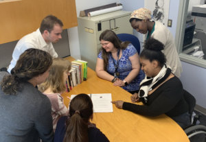 A diverse group of RespectAbility Fellows sitting and standing around a table looking at a document together