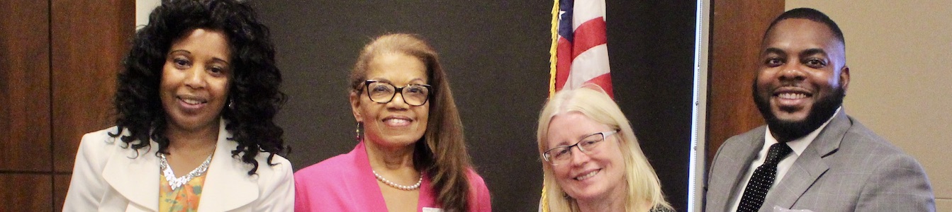 L-R: Janet LaBreck, Janie Jeffers, Diane Smith Howard, and Robert Stephens smiling in front of a wall and an American flag