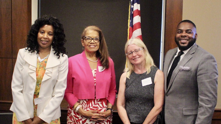 L-R: Janet LaBreck, Janie Jeffers, Diane Smith Howard, and Robert Stephens smiling in front of a wall and an American flag