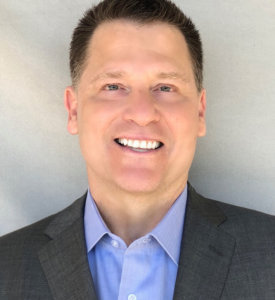 Jonathan Koch smiling wearing a suit in front of a grey backdrop