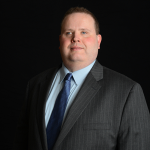 Gary Norman smiling wearing a suit and tie in front of a black background