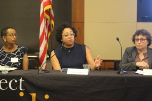 Evelyn Kelly speaking as Laka Mitiku Negassa and Ila Eckhoff look on. All are sitting behind a table with RespectAbility's logo on the tablecloth and in front of an American flag