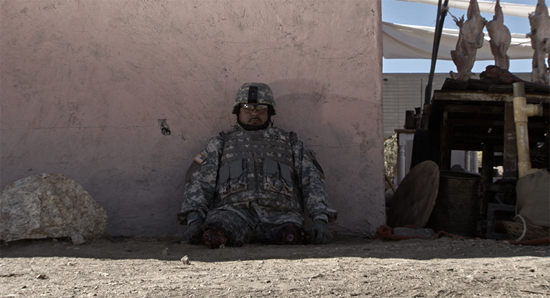 Still from Fort Irwin with Cristian Valle in a military uniform sitting outside leaning against a wall. Christian is a double amputee, and has no legs.