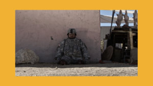 Still from Fort Irwin with Cristian Valle in a military uniform sitting outside leaning against a wall. Christian is a double amputee, and has no legs.