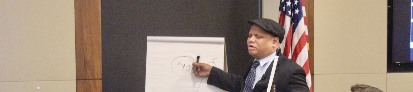Ollie Cantos writing on a flip chart holding a walking stick. American flag in the background