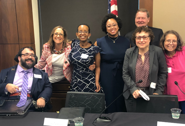 Self Advocacy Panelists smiling with Debbie Fink and Steve Bartlett in front of an American flag and behind a table