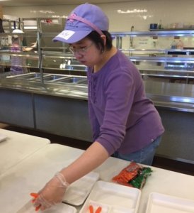 A CHAI Works-South participant wearing a purple shirt and hat inside a kitchen preparing lunch at The Rashi School in Dedham, MA.