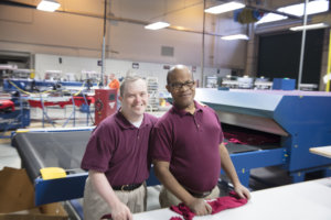 Two Bank of America Support Services employees smiling together inside a factory-like setting