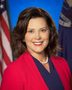 Governor Gretchen Whitmer smiling in front of an American flag and a Michigan state flag