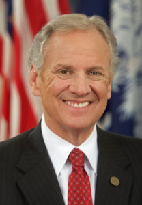 Governor Henry McMaster smiling in front of an American flag.