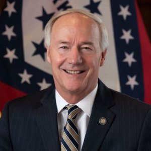 Arkansas Governor Asa Hutchinson smiling in front of the state flag.