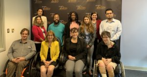 Debby Fisher with RespectAbility Staff and Fellows smiling in front of the RespectAbility banner