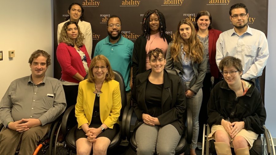 Debby Fisher with RespectAbility Staff and Fellows smiling in front of the RespectAbility banner