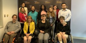 Debby Fisher with RespectAbility Staff and Fellows smiling in front of the RespectAbility banner