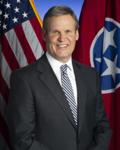 Tennessee Governor Bill Lee smiling in front of the state flag and an American flag