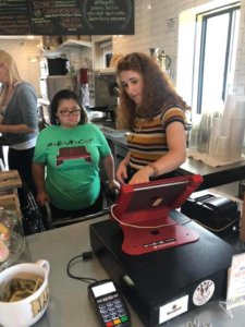 An employee training their coworker with a disability on the register